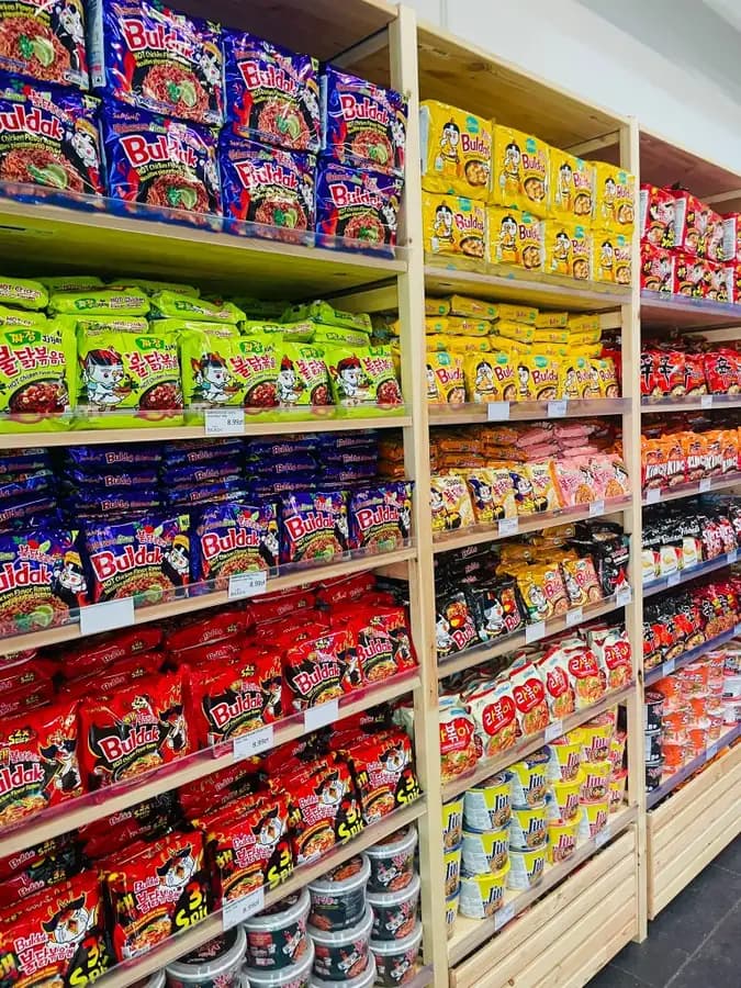 Samyang Buldak hot chicken ramen packs on wooden shelves at OKASHI Group Asian supermarket