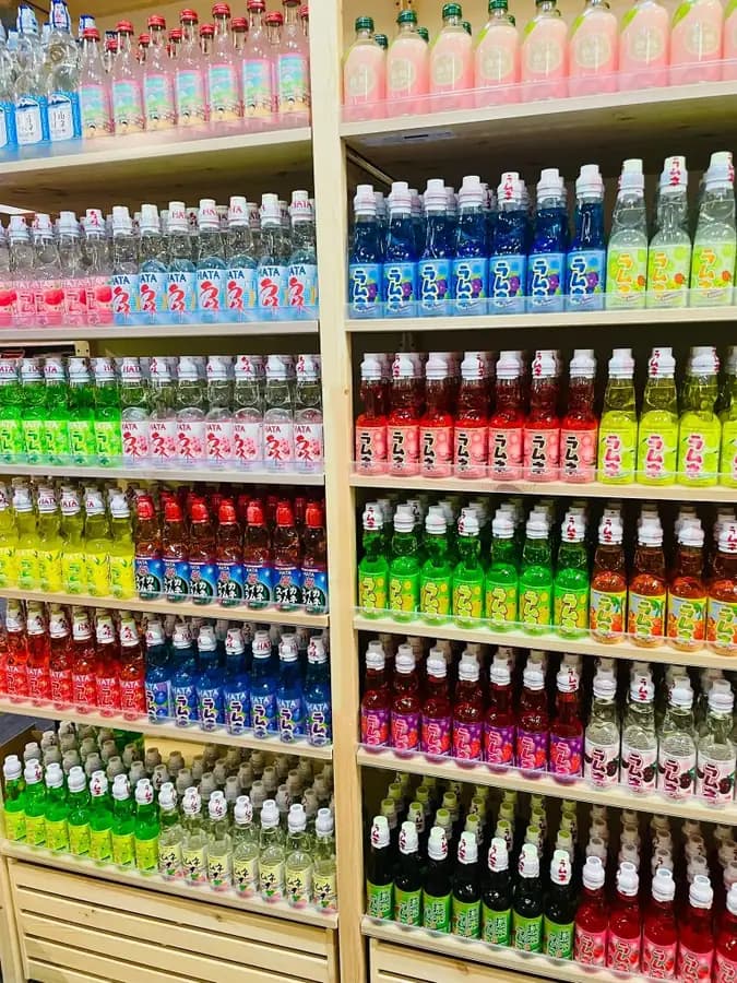 Rows of Japanese Ramune soda bottles on wooden shelves in the OKASHI Group supermarket