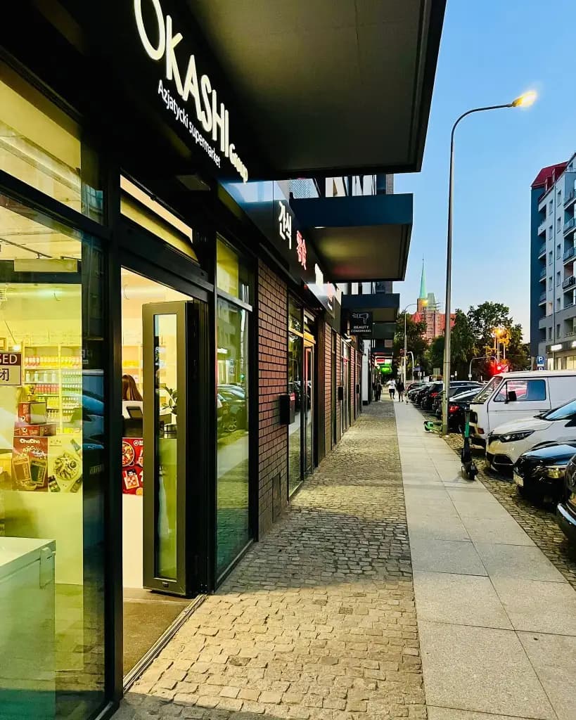 OKASHI Group storefront at dusk on Świętokrzyska, Wrocław — Asian supermarket glass entrance